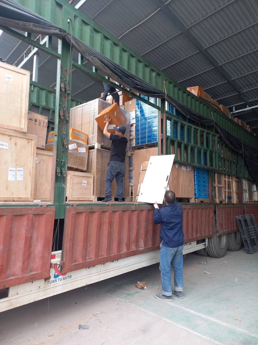Nhân công chuyển thùng gỗ và kiện hàng lên xe tải thùng dài trong nhà xưởng